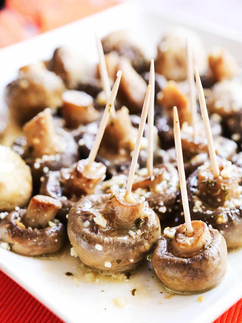 Cooked mushrooms lined up on serving plate, with toothpicks in each one.