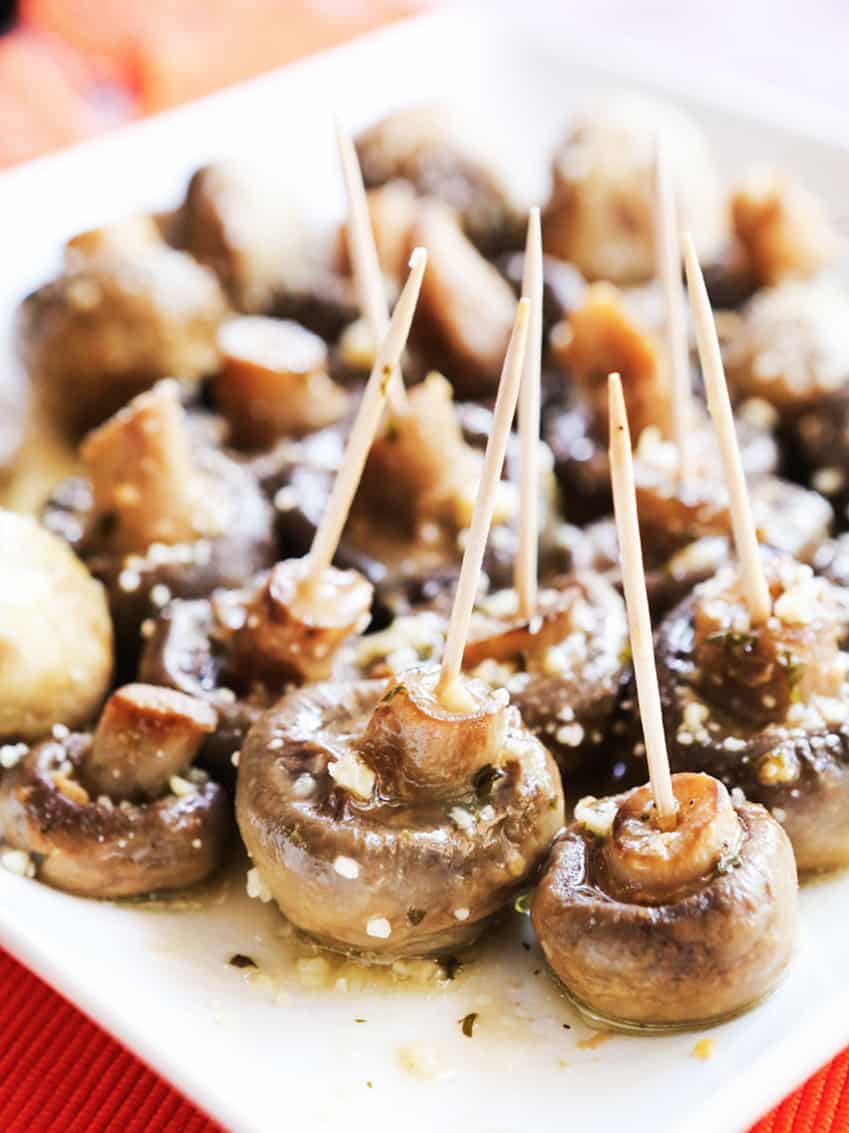 Cooked mushrooms on a serving plate with toothpicks stuck inside each one.