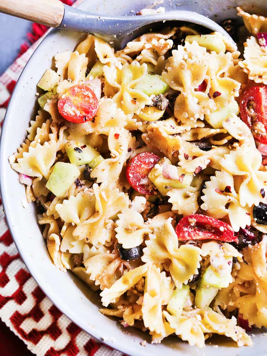 Bowl of Mediterranean pasta salad in a bowl with a wooden spoon tucked in. 