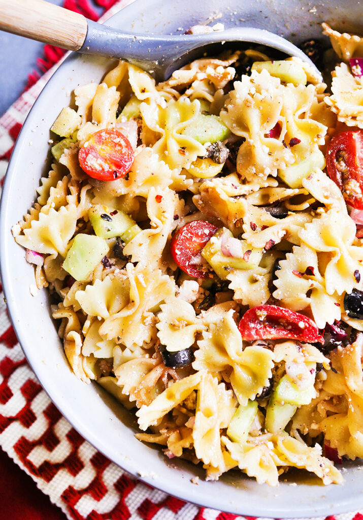 Mediterranean pasta salad ready to serve in a bowl with a serving spoon. 