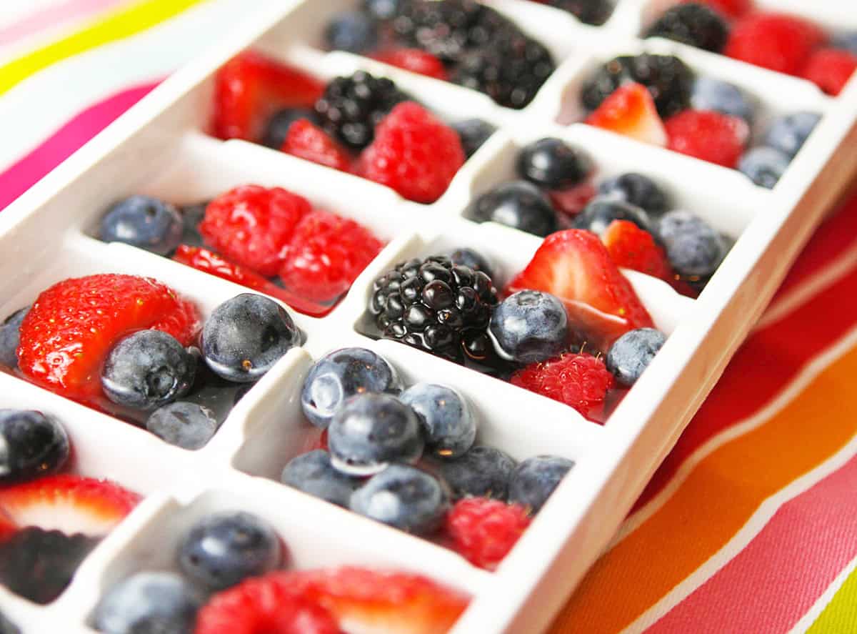 Ice cube tray filled with mixed berries and water, ready to freeze.