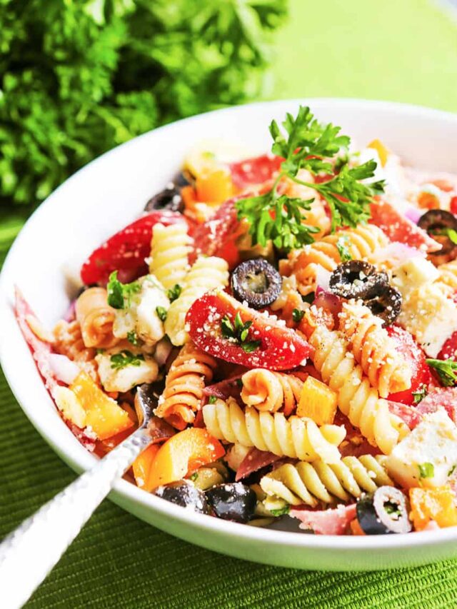 Italian pasta salad in a bowl with a serving spoon resting in it. 