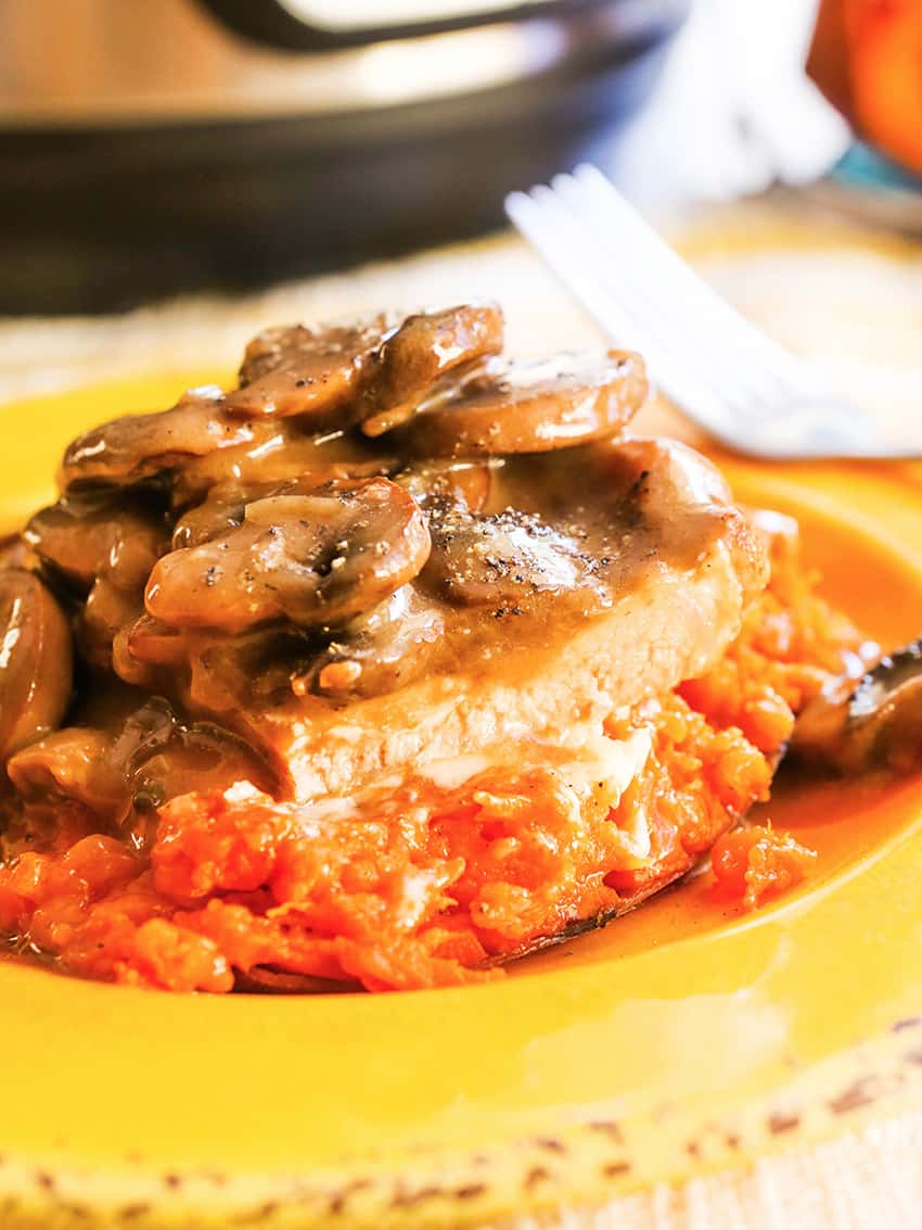 Pork chops with gravy and mushrooms topping it on a plate. 