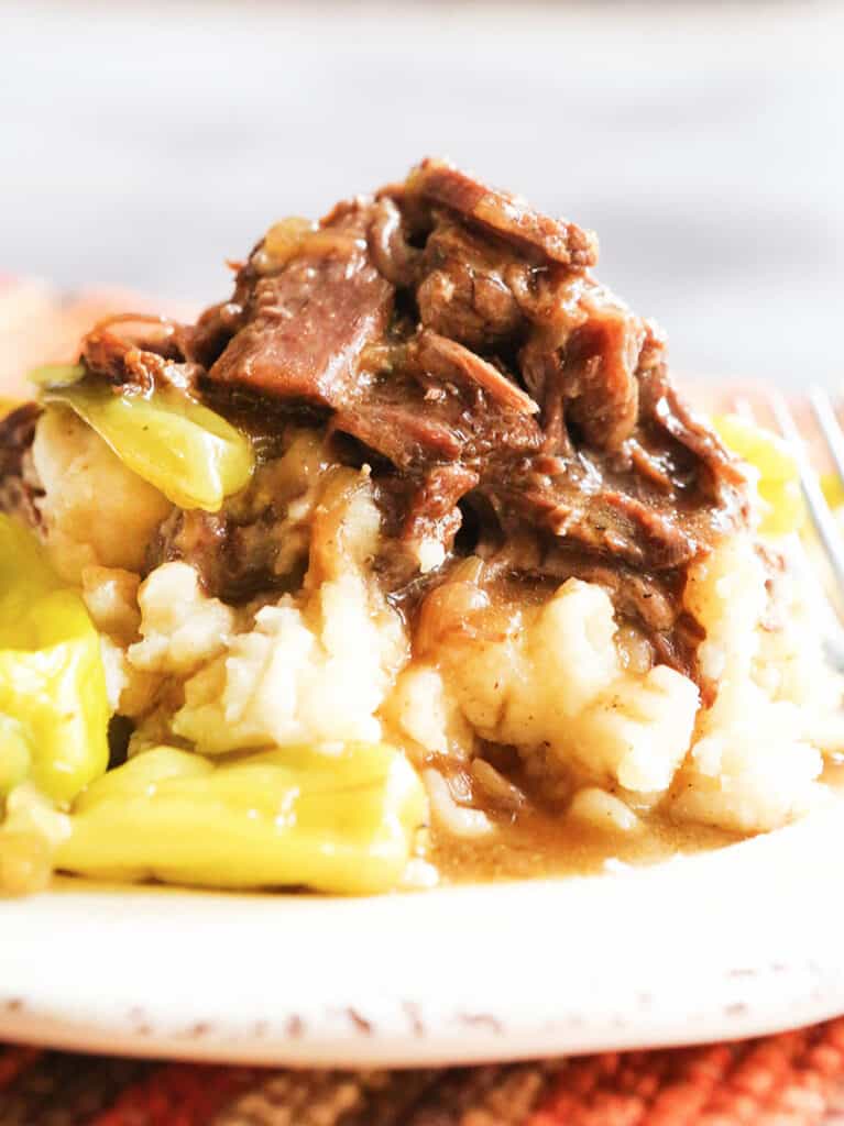 Instant pot mississippi roast on a plate topping a pile of mashed potatoes with peppers on the side of the plate. 