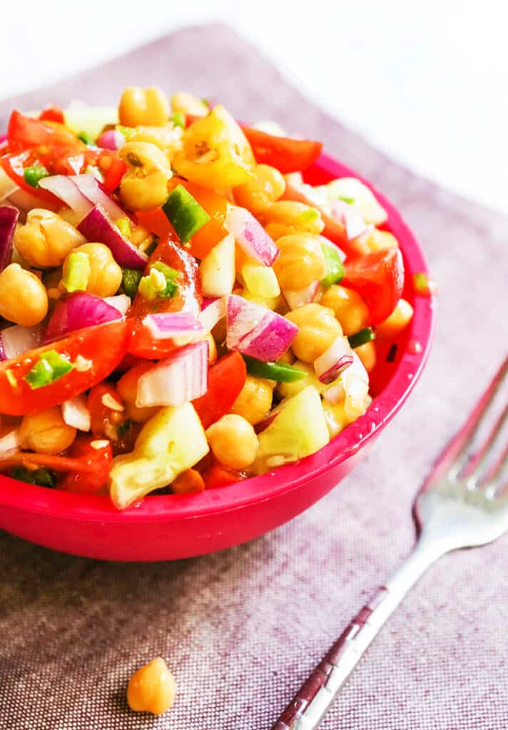 spicy chickepea salad in a red bowl with a fork alongside it. 