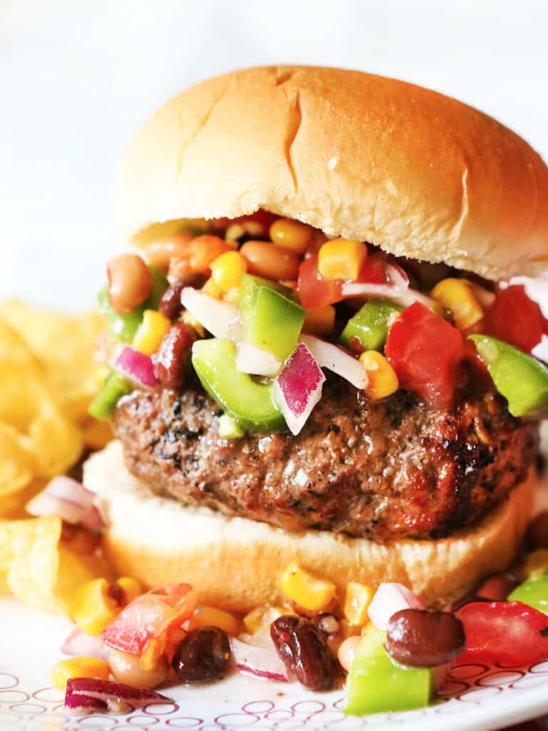 Loaded hamburger topped with salsa on a plate.