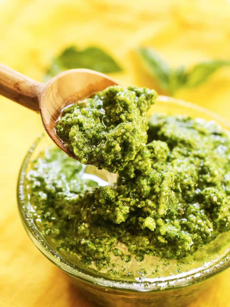 Wooden spoon lifting fresh pesto out of a glass bowl.