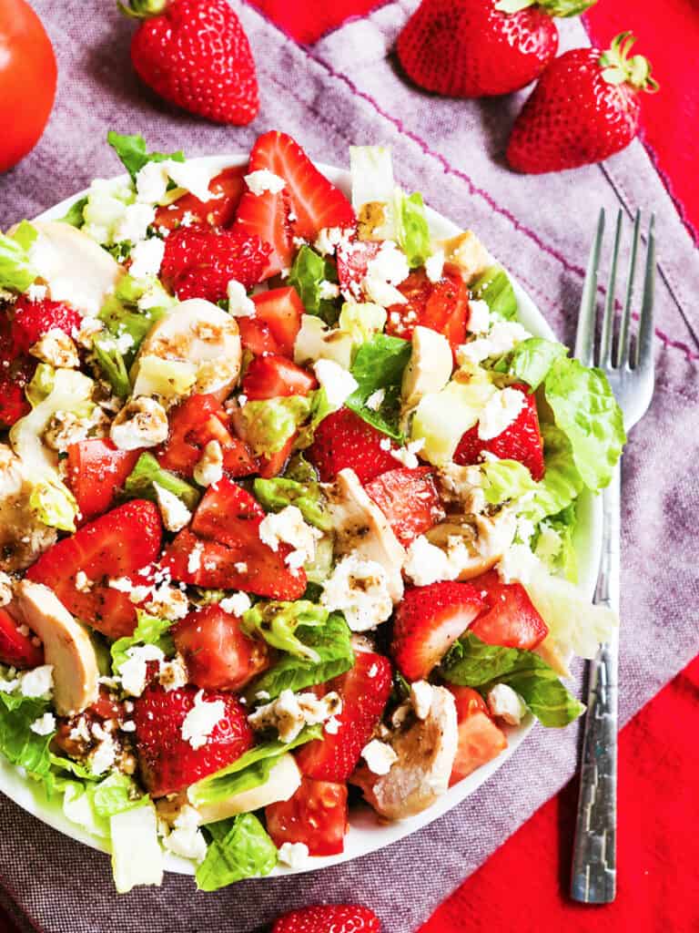 Plate full of strawberry balsamic chicken salad on a tablecloth with a fork alonside.