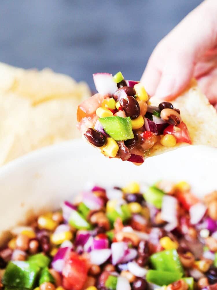 Hand holding a tortilla with a scoop of Spicy Bean Salsa on it. 