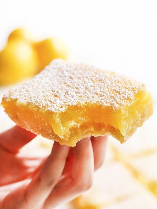 Hand holding a lemon bar slice with a bite missing. 