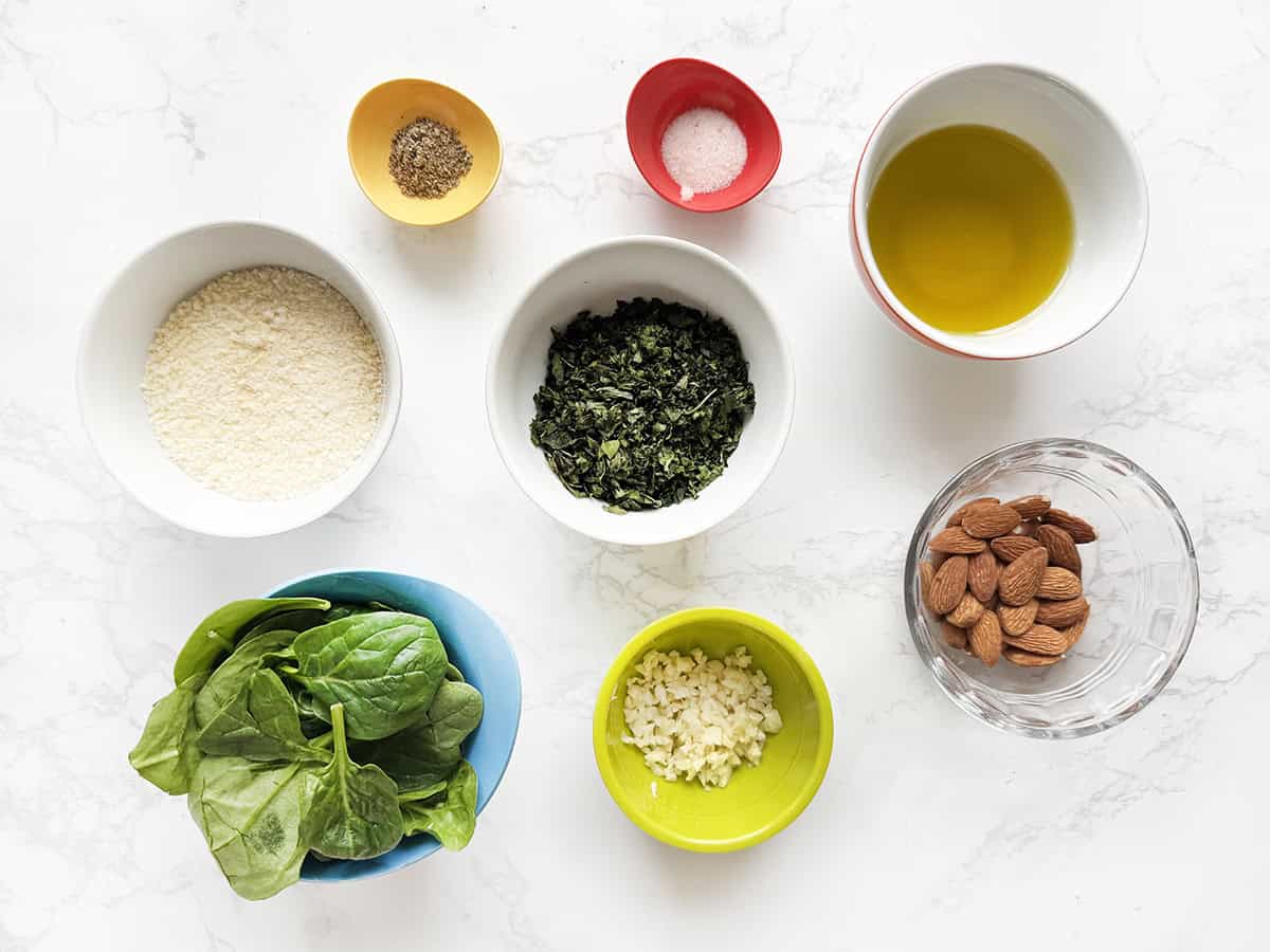 Ingredients for homemade almond pesto in individual bowls, lined up on a white counter.