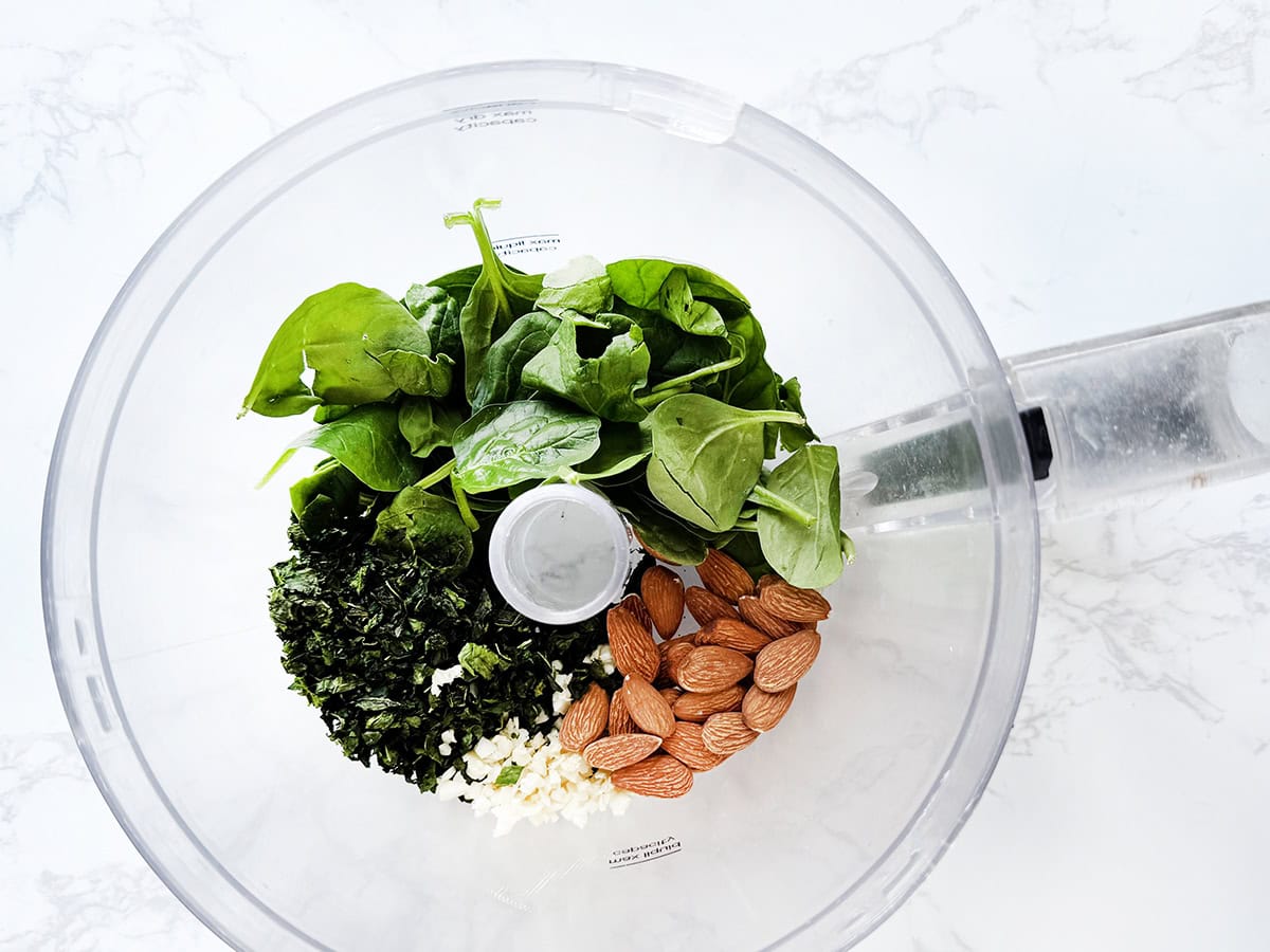 Spinach, basil, almonds and garlic in the bowl of a food processor.