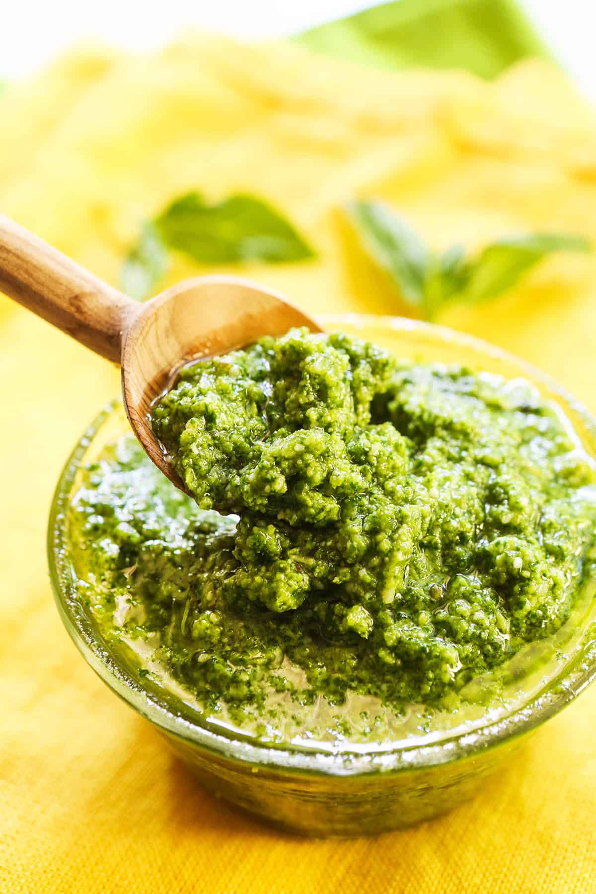 Small wooden spoon lifting a spoonful of pesto out of a glass dish.