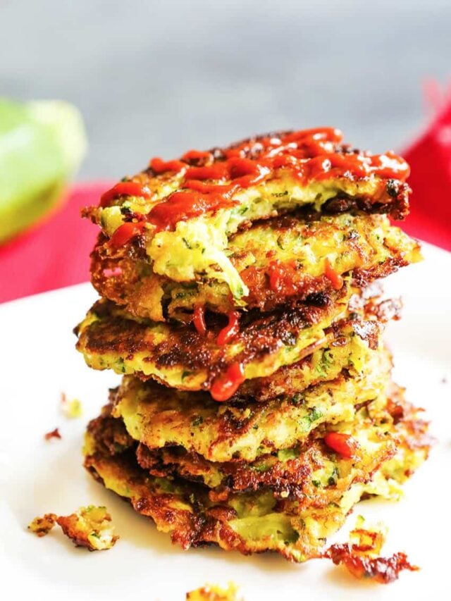 Stack of zucchini fritters with ketchup drizzled over the top. 