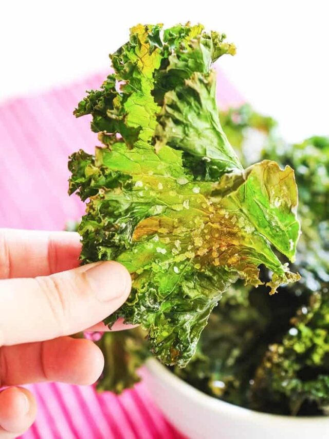 Hand holding up a kale chip with sea salt on it. 