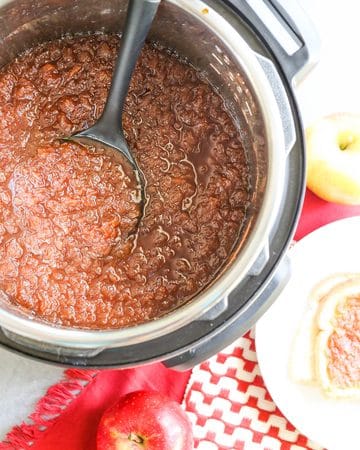 Cooked apple butter in an Instant Pot with a ladle, apples and bread on the side.