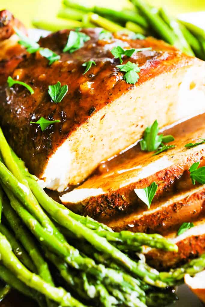 instant pot turkey breast sliced with gravy drizzled over it on a platter with a side of asparagus