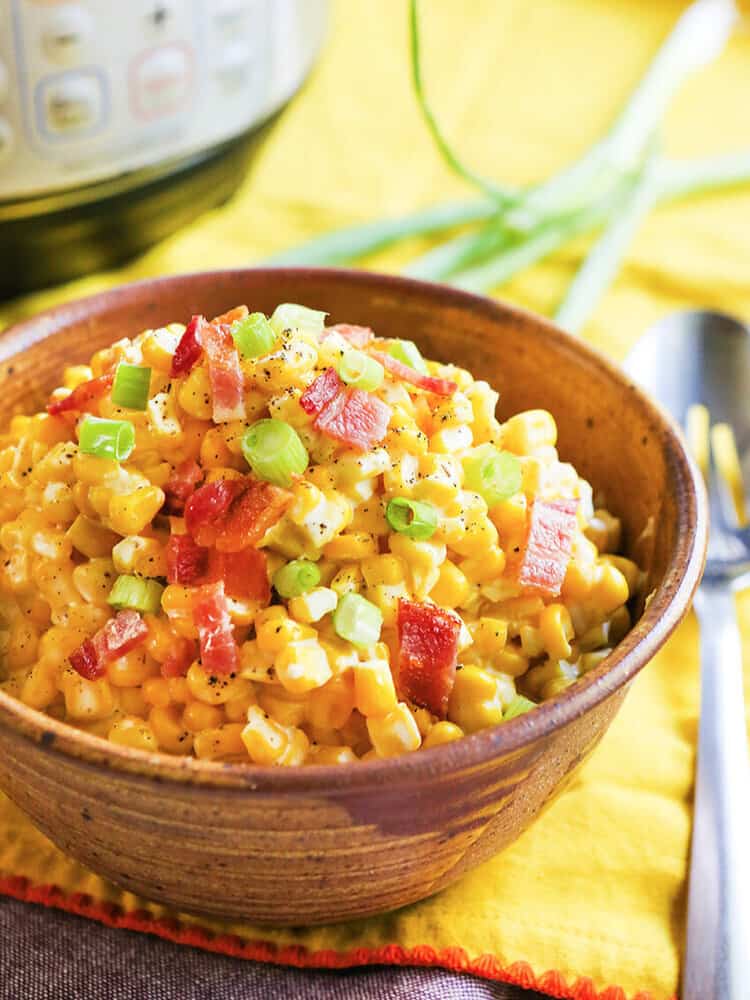 Creamed corn in a serving bowl with a large serving spoon on the side. 