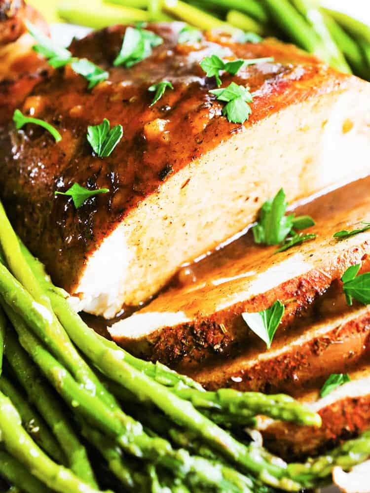 a turkey breast with several slices cut open and gravy poured over the top with asparagus on the side.  