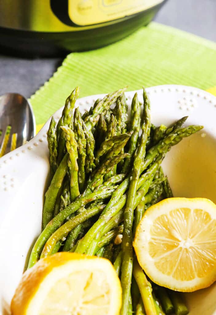 serving bowl with instant pot asparagus inside with 2 slices of lemons sitting on top 