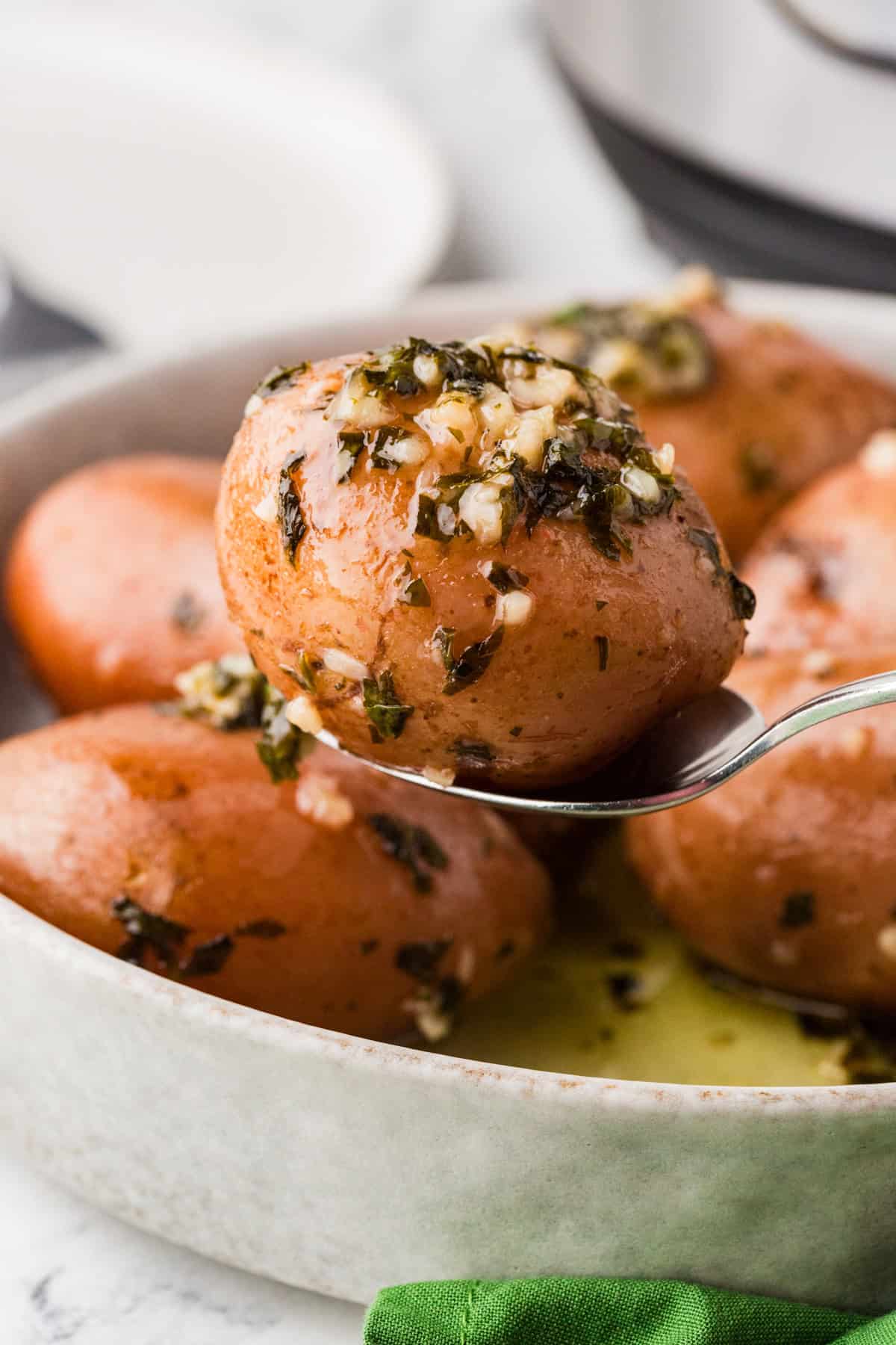 Spoon holding up one potato covered with parsley and garlic, hovering above serving dish.