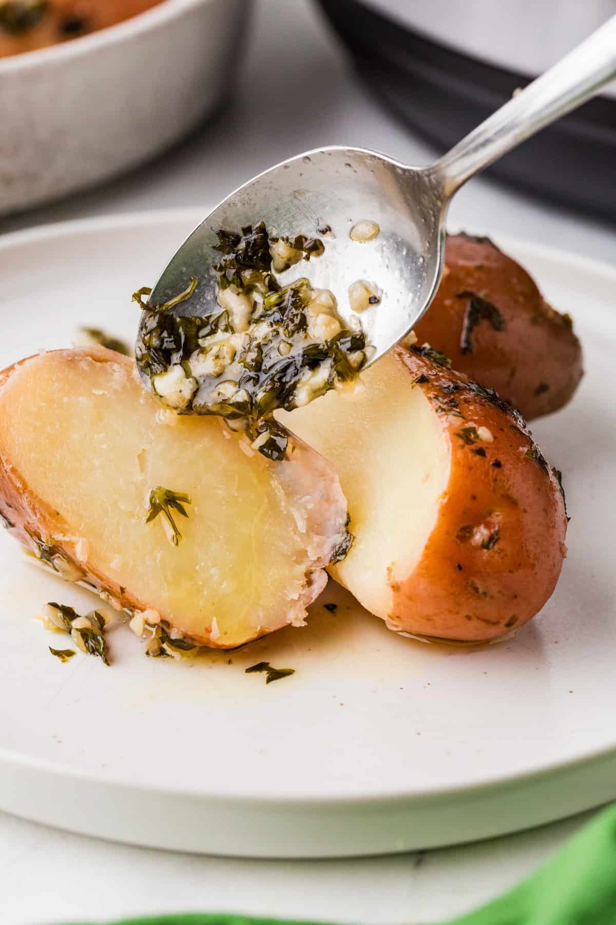 Spoon drizzling garlic sauce over a potato that has been cut in half.