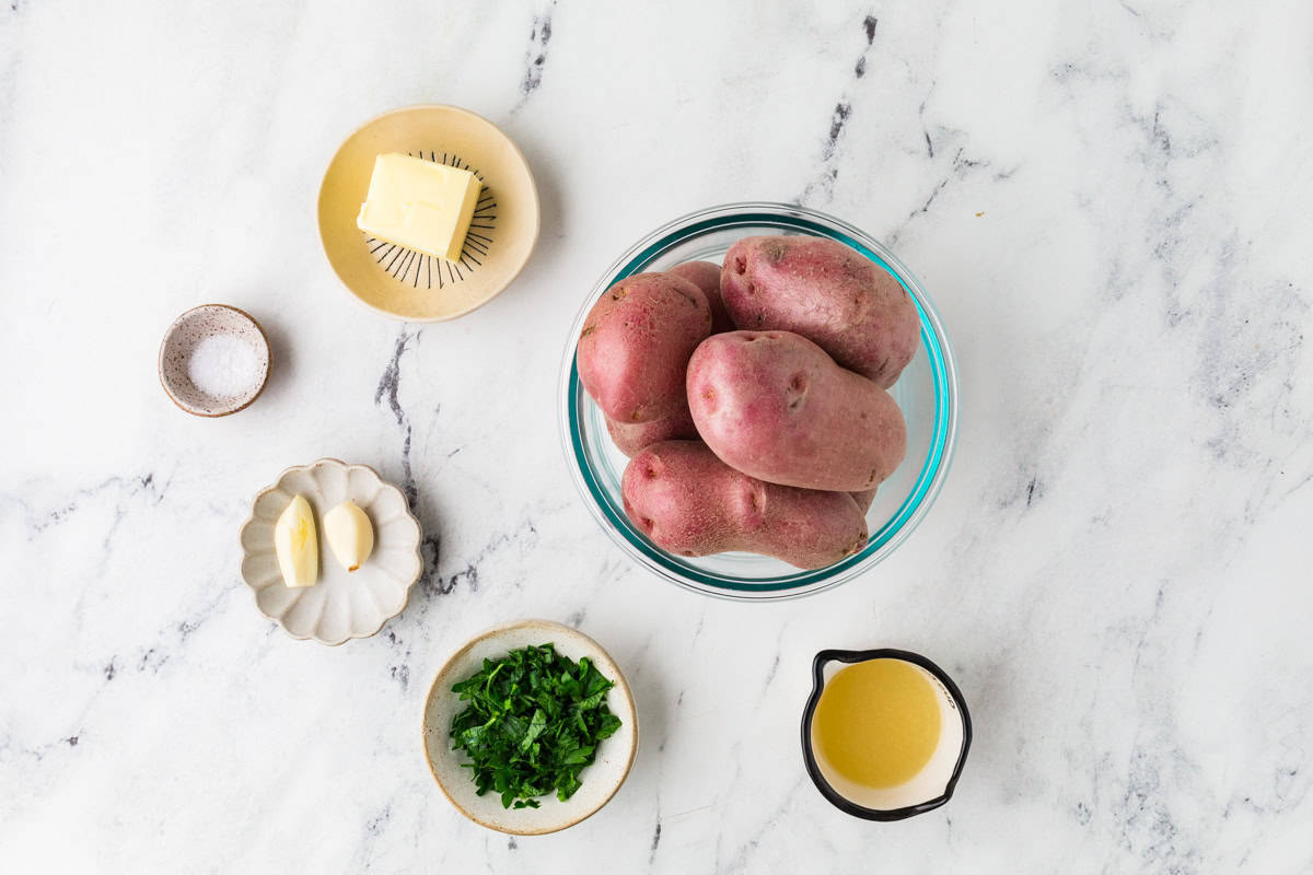 Ingredients for a red potato side dish in bowls on a white counter.