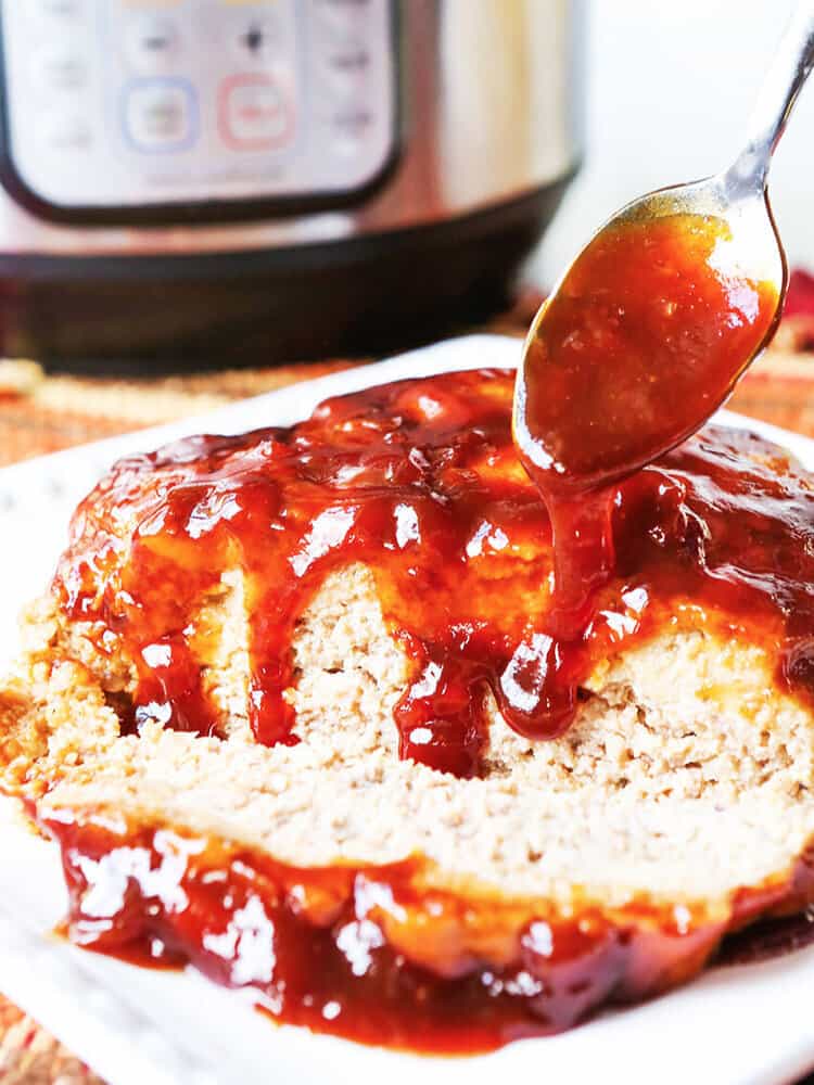 meatloaf with a spoon drizzling sauce over it on a platter in front of an instant pot