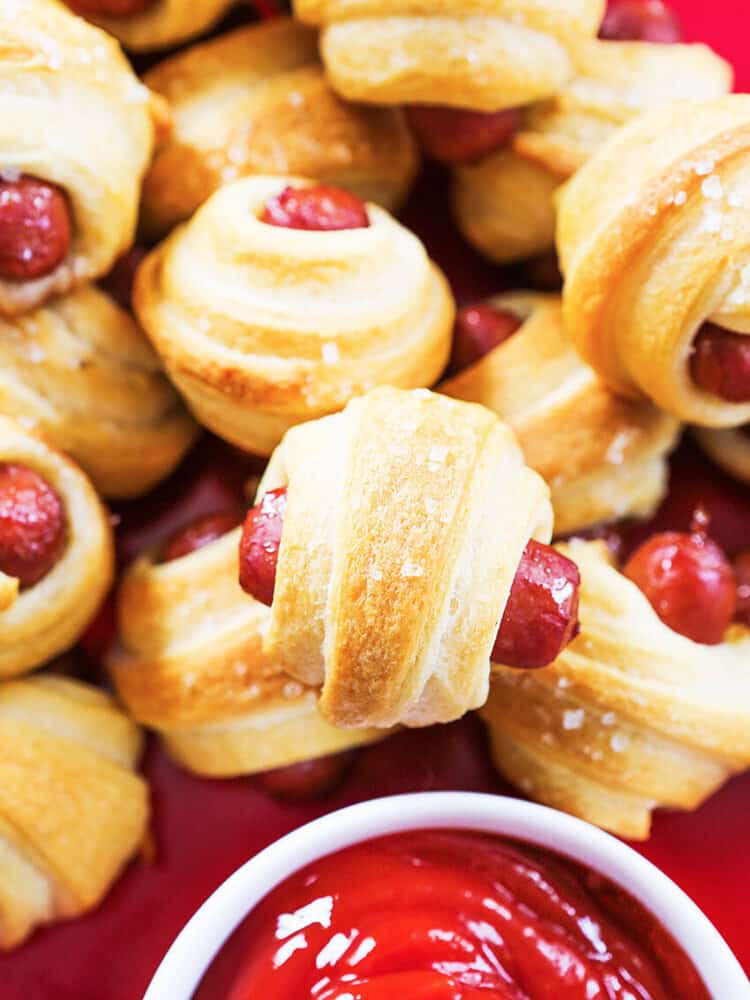 Pigs in a blanket stacked up next to a small bowl of pigs in a blanket. 