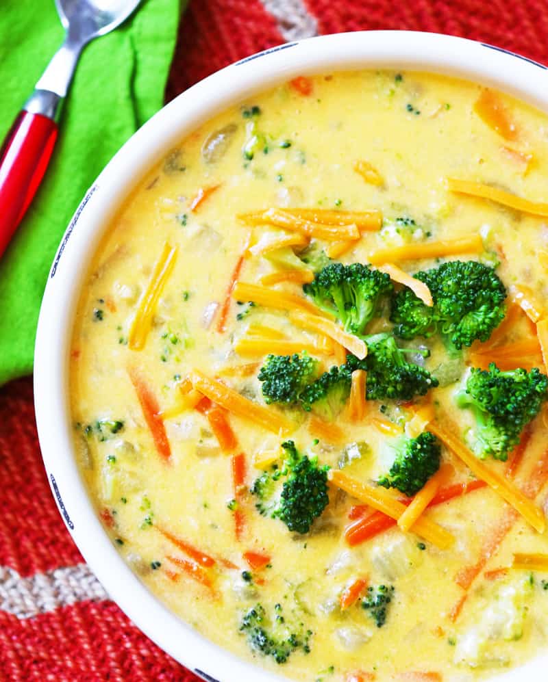 Broccoli cheese soup served in a white bowl with chopped pieces of broccoli and grated cheese garnished on top. 