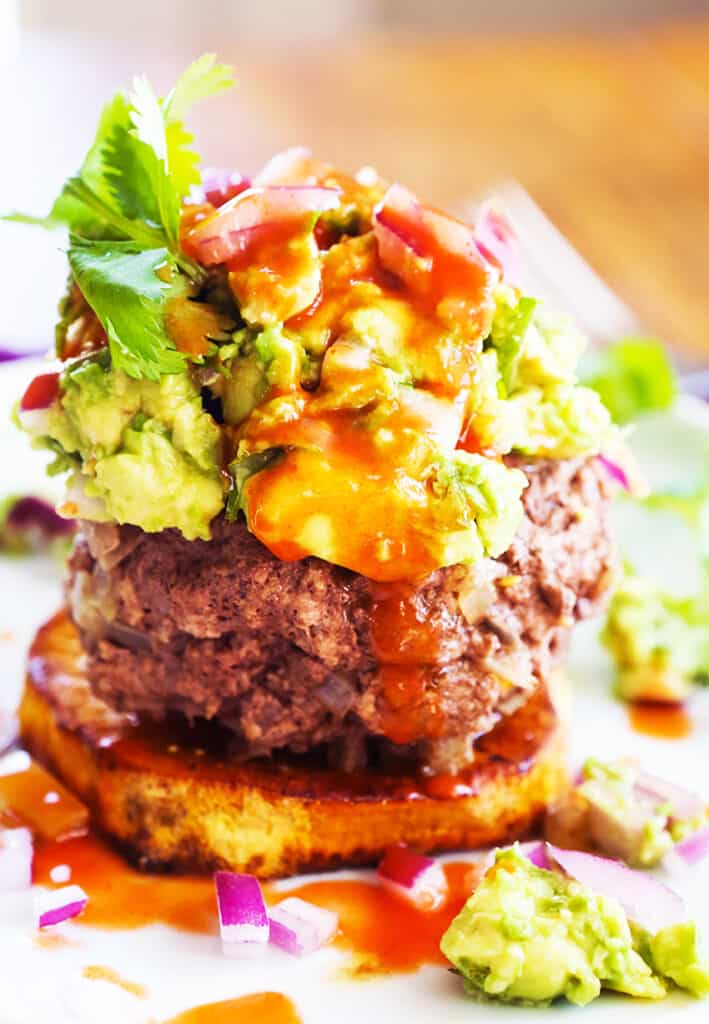Burger sitting on a sweet potato bun and topped with guac and hot sauce.