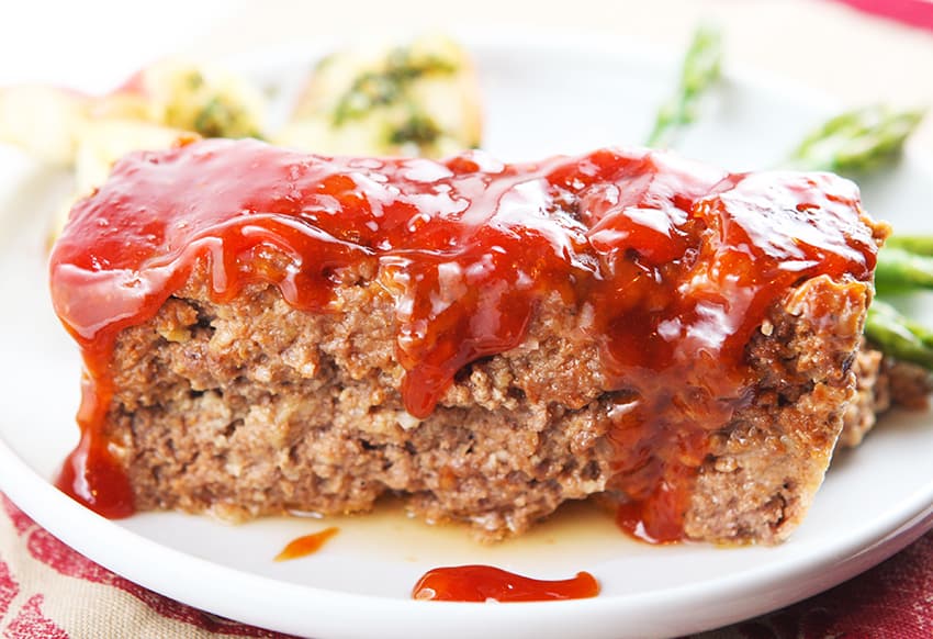 perfect slice of meatloaf on a white plate with sauce dripping down sides.