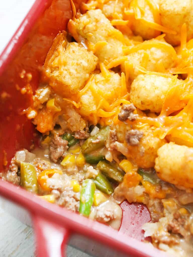 cheesy tater tots with veggies and beef spilling out the bottom in a baking dish.