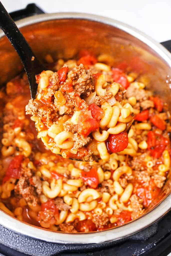 ladle full of cooked pasta, tomatoes and meat being lifted out of an Instant Pot.