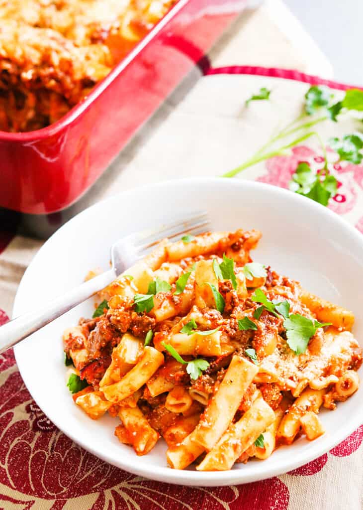 Plate of baked ziti sitting next to baking dish.