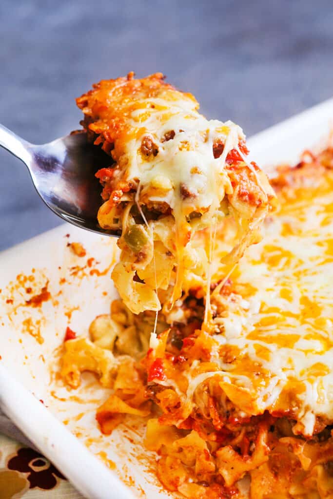 Cheesy spoonful of noodles being scooped out of a baking dish.