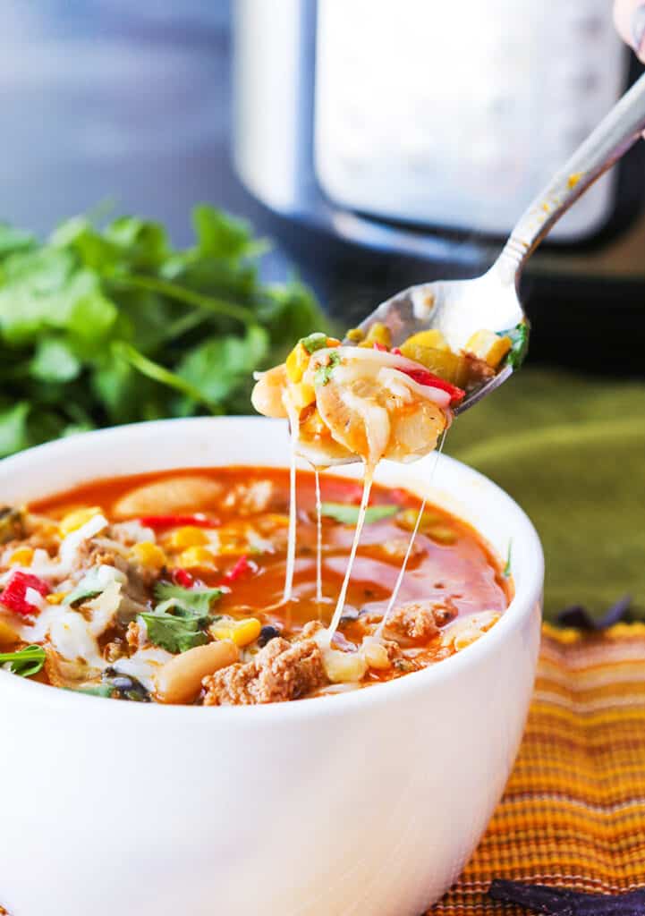 Spoon full of turkey chili coming out of a bowl with cheese pulls sitting in front of an Instant Pot. 