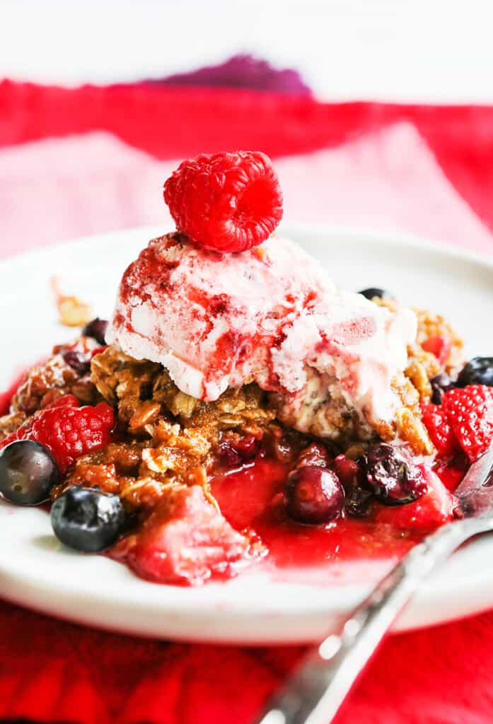 plate of berry crisp with a scoop of ice cream on top and a raspberry garnish