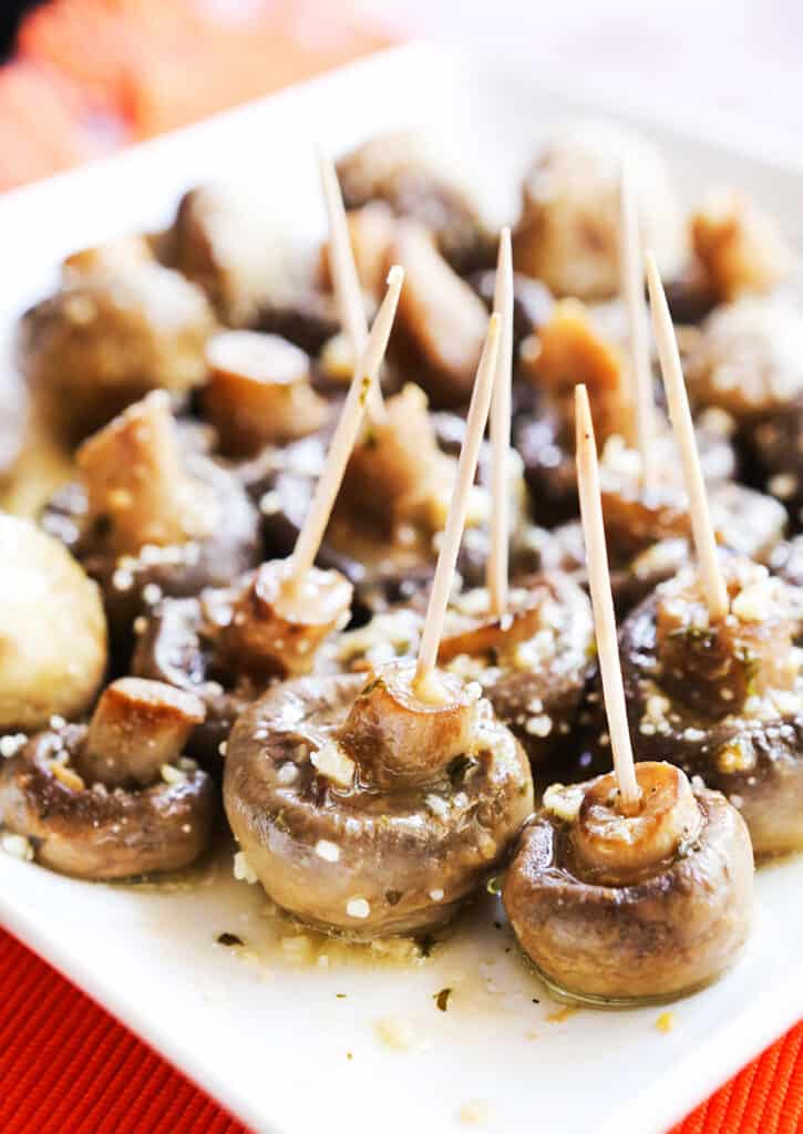 Toothpicks in mushrooms prepared in butter ranch sauce sitting on a serving tray. 