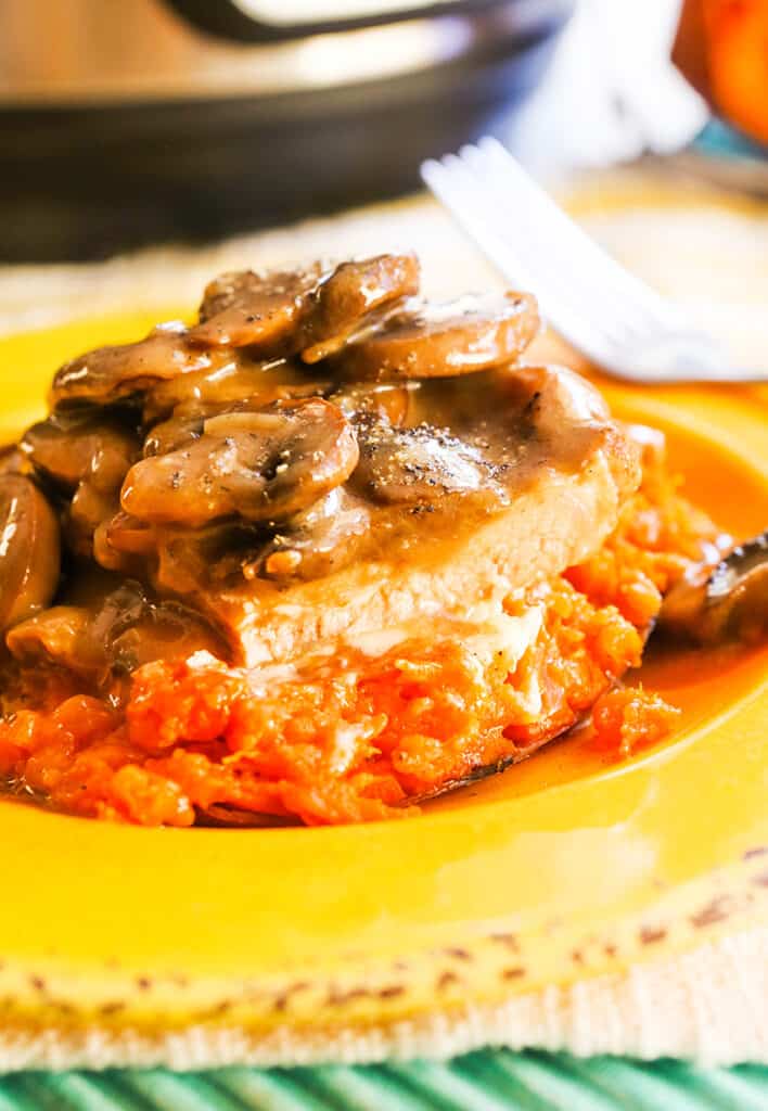 Plate of pork chops with gravy and mushrooms topping it sitting in front of an Instant Pot. 