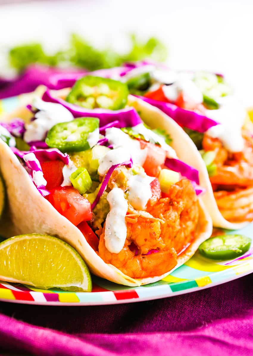 Shrimp tacos in flour tortillas on a plate with lime wedges. 