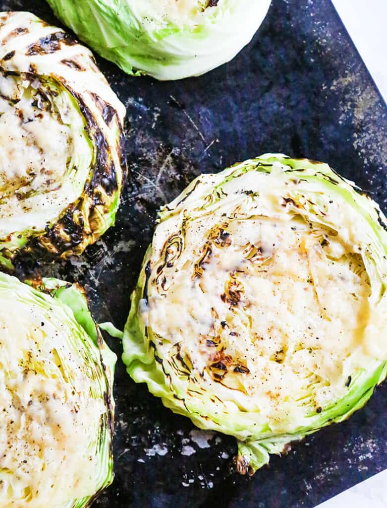 Cabbage steaks with melted cheese on top and lined up on a baking sheet.