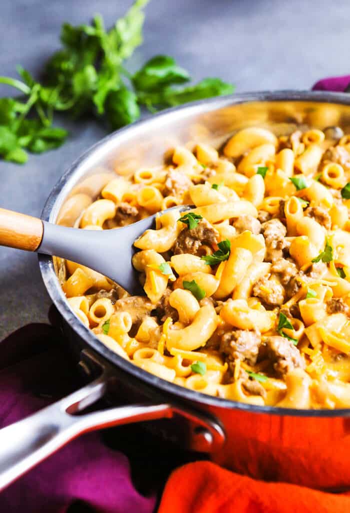 serving spoon sticking into skillet of cooked elbow macaroni and beef.