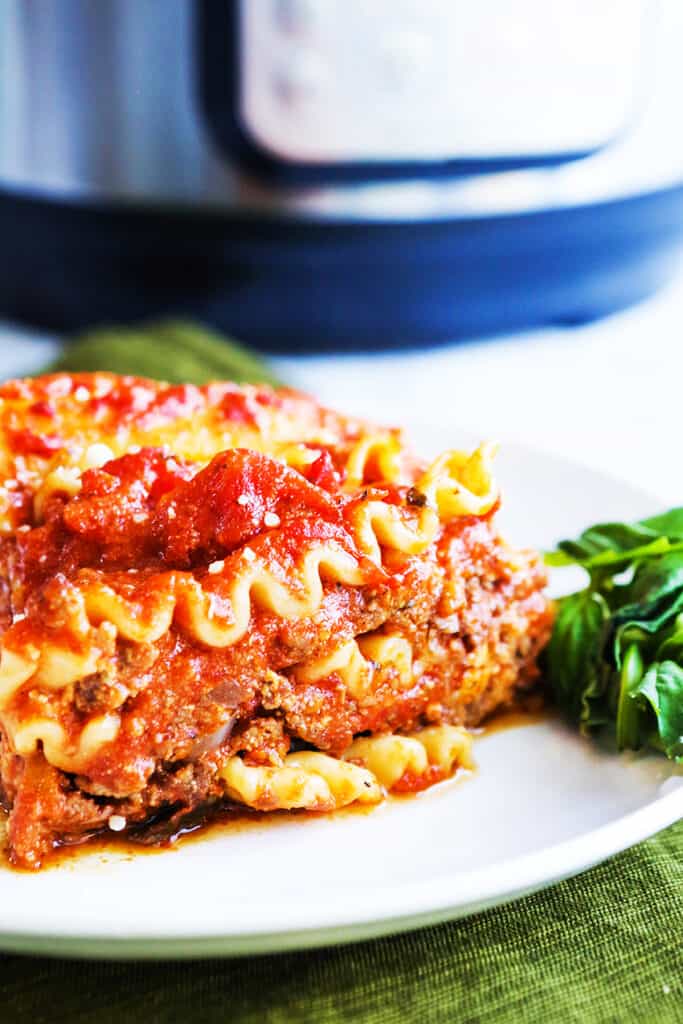 Perfectly stacked piece of lasagna on a white plate sitting next to an Instant Pot.