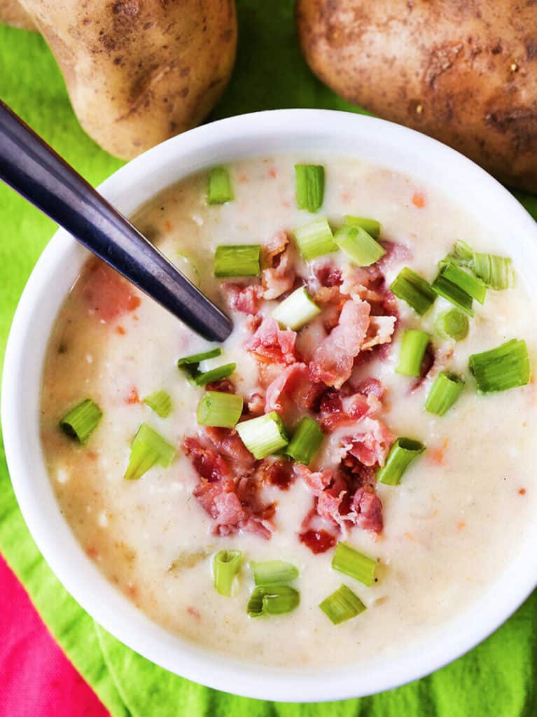 Bacon bits and diced green onions in a bowl of potato soup. 