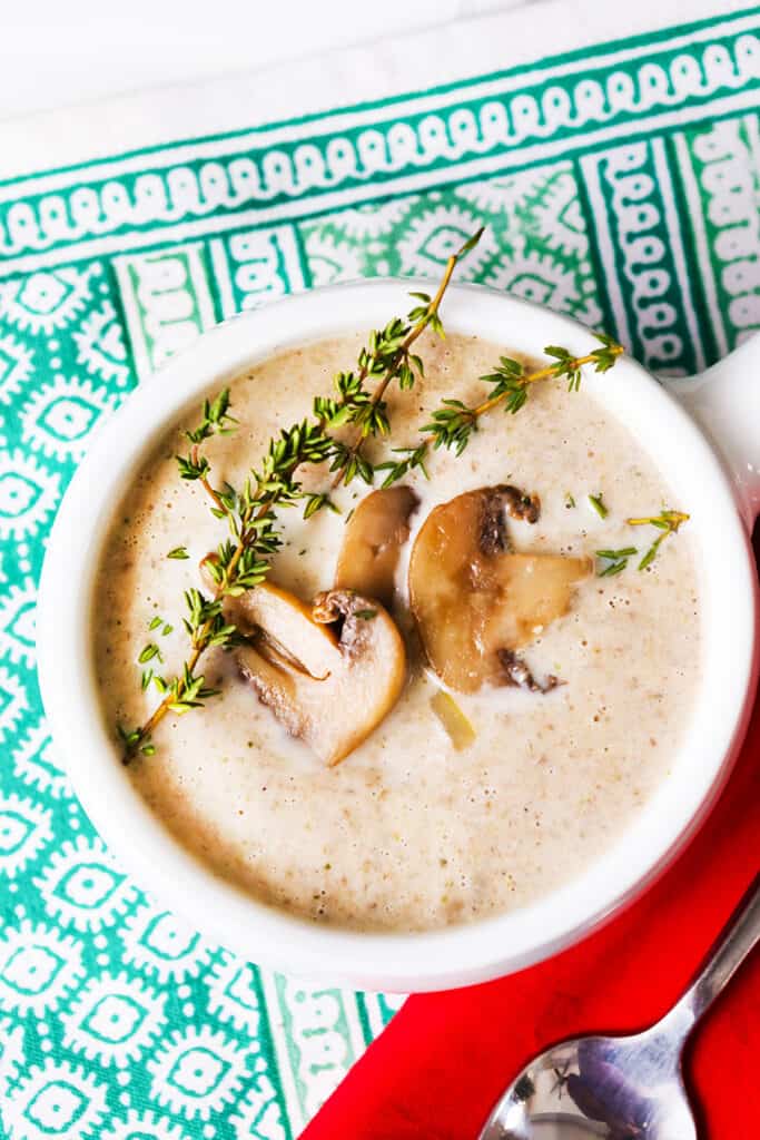 A bowl of creamy mushroom soup with a sprig of thyme and fresh mushrooms on the top. 