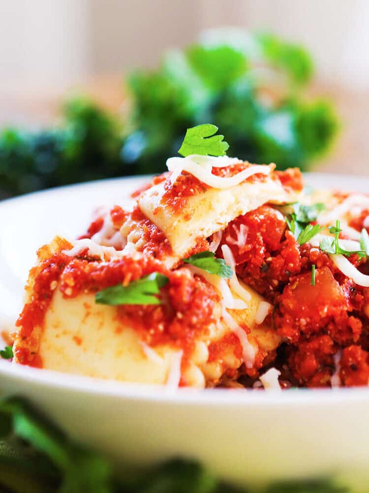 Cheesy ravioli piled high on a plate and covered with a meaty red sauce.