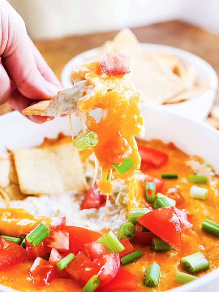 Hot crab dip on a chip with melted cheese pulling out of the baking dish. 