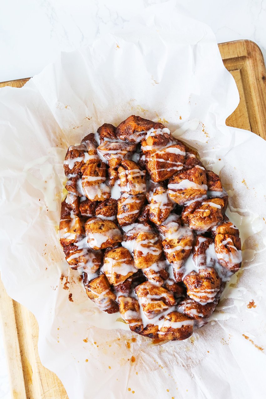 Crock pot cinnamon roll monkey break drizzled with simple icing in a bed of parchment paper. 