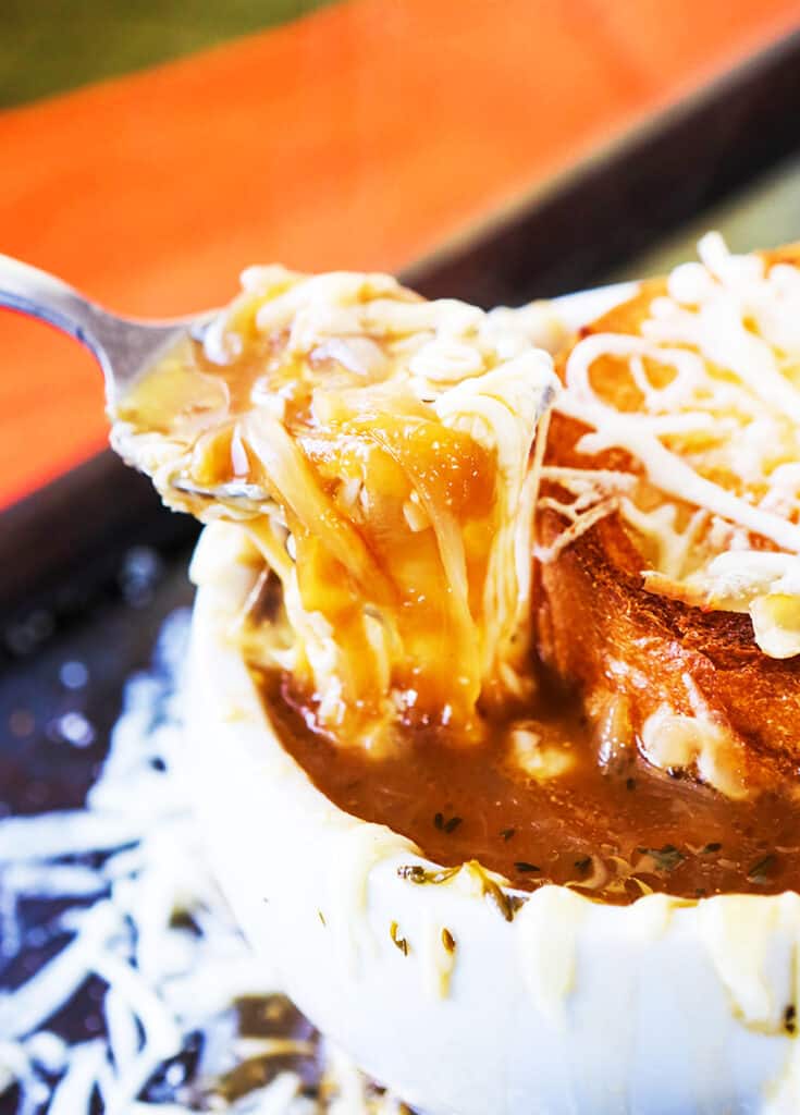 A spoonful of gooey cheese pulling out from a soup bowl of french onion soup. 